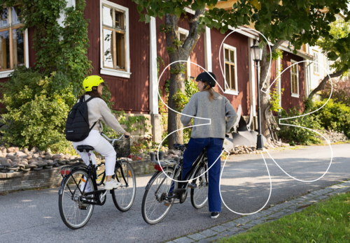 Kaksi pyöräilijää Naantalin Vanhassakaupungissa lähdössä liikkelle. Onnellinen aurinko -elementti.