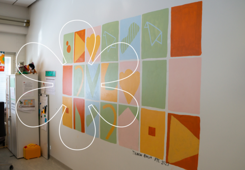 Seinälle on maalattu kolmeen riviin neliöitä, joiden sisällä on erilaisia muotoja. Kuvan päällä Onnellinen aurinko -elementti.