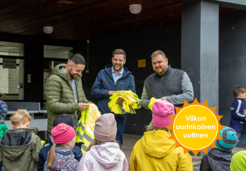 Kolme iloista miestä seisoo lapsiryhmän edessä ja jakaa keltaisia heijastinliivejä.