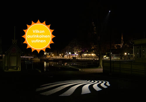 Valo heijastaa aaltoilevat säteet maahan pimeässä Vanhankaupungin rannassa. Taustalla näkyy Naantalin rantaravintolat ja kirkko.Viikon aurinkoinen uutinen.
