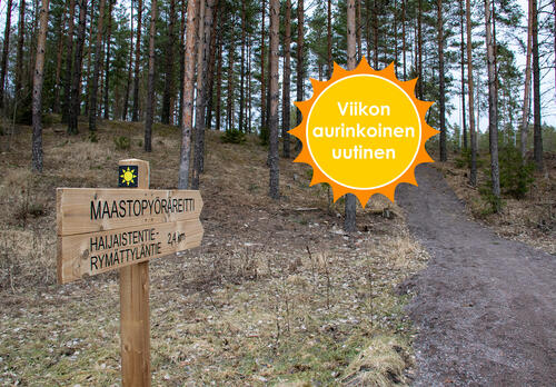 Aurinkologolla varustetussa kyltissä lukee: Maastopyöräreitti Haijaistentie-Rymättyläntie, 2,4 km. Kyltit osoittavat ylämäkeen, joka vie metsään. Viikon aurinkoinen uutinen