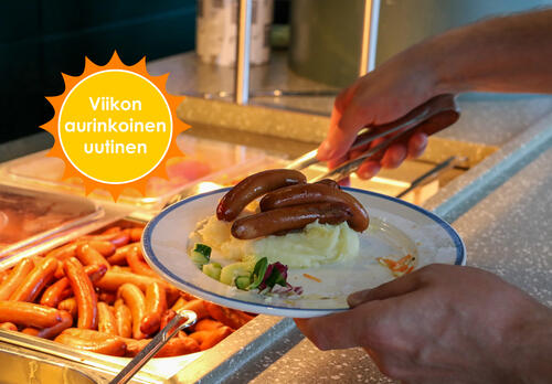 Henkilö ottaa linjastolla lautaselleen nakkeja, kädet ja lautanen, jossa on perunamuusia ja nakkeja, näkyvät kuvassa.