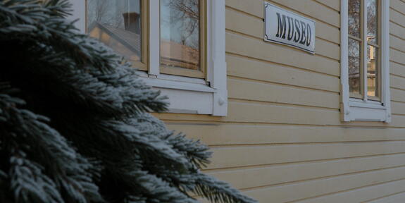 Humpin portaiden kaide, jossa kuusen oksia. Taustalla keltainen seinä ja Museo-kyltti.