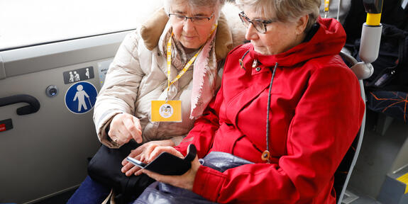 Kaksi seniorinaista tutkii bussissa puhelinta.
