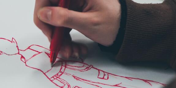 Käsi piirtää Manga-hahmoa punaisella kynällä, päällä musta paita.