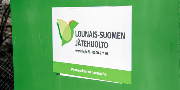 Vihreässä jäteastiassa valkoinen tarra, jossa teksti: Lounais-Suomen Jätehuolto, www.lsjh.fi, 0200 47470, Pienempi kuorma huomiselle. 