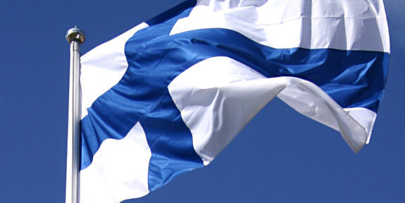Suomen lippu liehuu vasten sinistä taivasta.