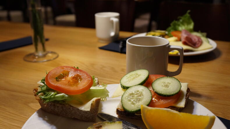 Pöydällä lautanen, jossa on leipiä ja appelsiinia, sekä kahvikuppi.