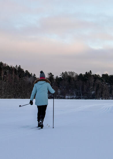 Vaaleansiniseen talvitakkiin pukeutunut hiihtäjä hiihtää ladulla järven jäällä.