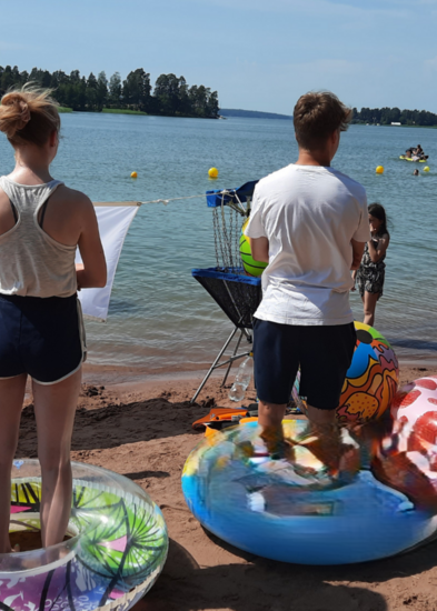 Kolme nuorta seisoo rannalla uimarenkaissa