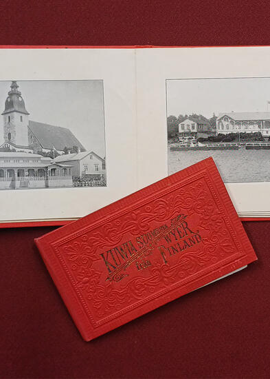 Punaisella taustalla avoin vihkonen, jossa kaksi mustavalkoista valokuvaa