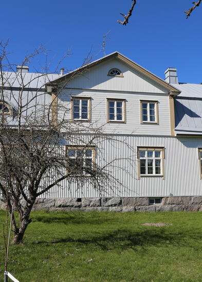 puinen, vaaleaksi maalattu rakennus, edustalla nurmikko 