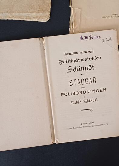 tummalla taustalla avoinna oleva kirja, jossa otsikko "Naantalin kaupungin poliisijärjestyksen säännöt"