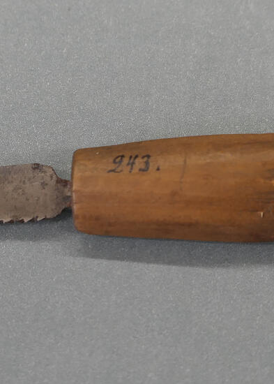 harmaalla taustalla vanha veitsen näköinen pieni saha, jossa puuvarsi