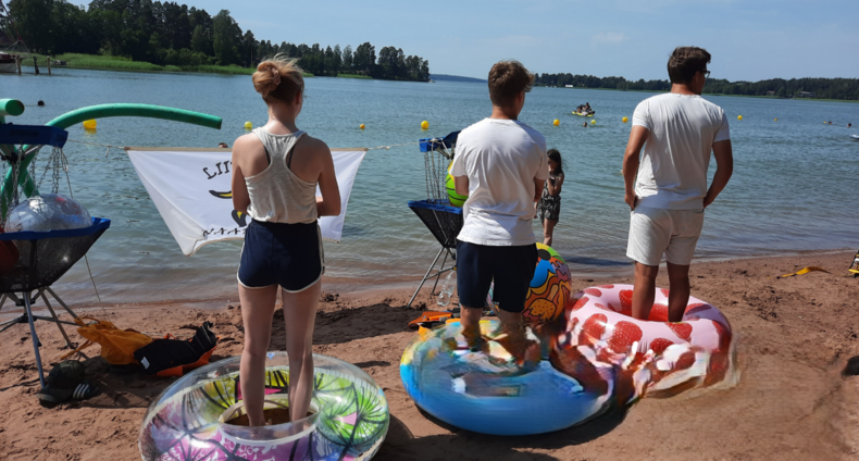 Kolme nuorta seisoo rannalla uimarenkaissa