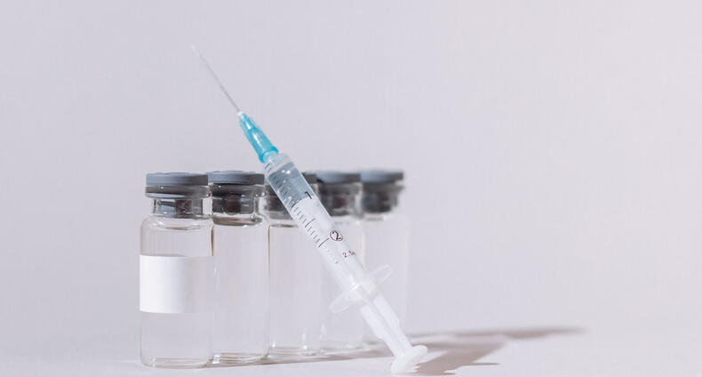 Rokotuspiikki nojaa rokotepulloihin pöydällä.